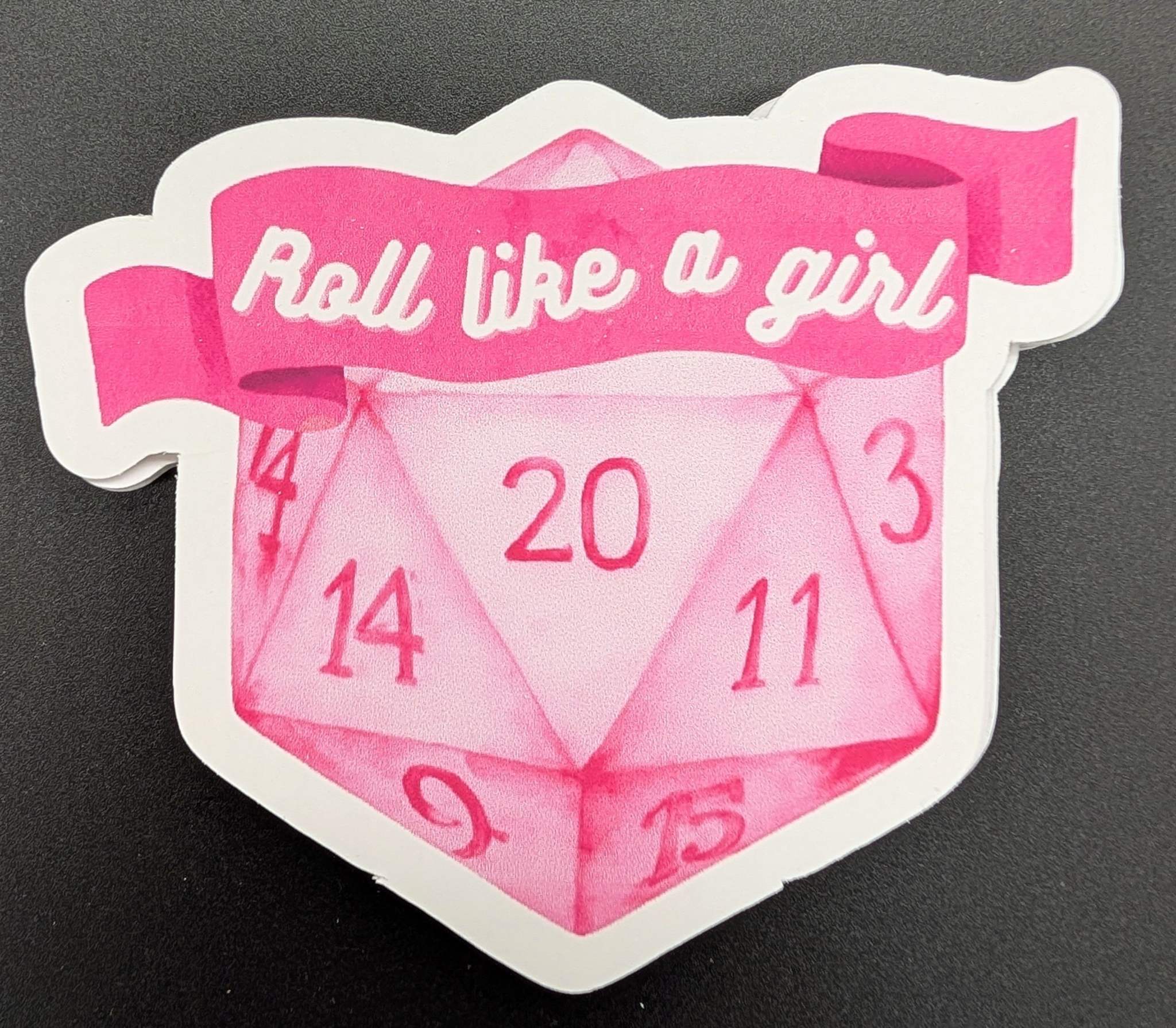 Sticker with D20 dice with a banner reading roll like a girl in pink