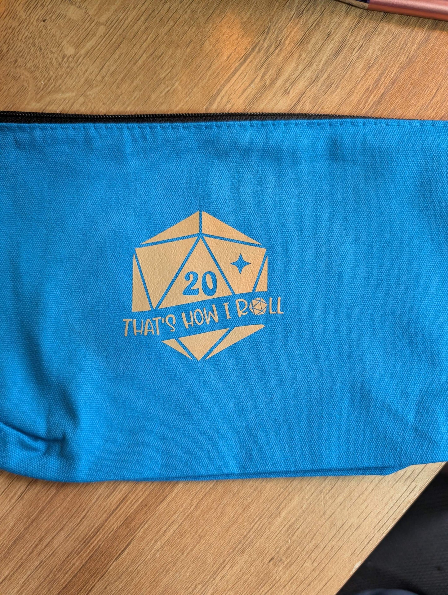 Zippered pouch with a D20 dice and words "that's how I roll"