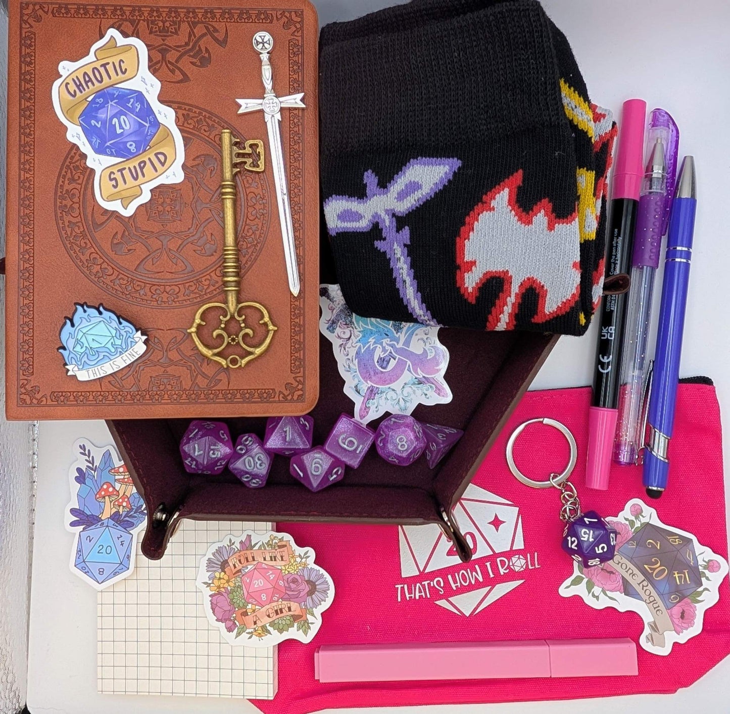 DnD Nerd Deluxe Bundle with faux leather notebook, dice set, pens, socks, stickers, keychain, and accessories on pink pouch